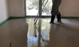 Pracownik wylewa betonową podłogę, sprawdzając, ile materiału potrzeba na m2.