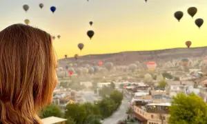 Kvinna ser på en magisk soluppgång över Kappadokien, Turkiet, med hundratals luftballonger som svävar i den gyllene himlen.