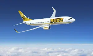Samolot Buzz, należący do Ryanair, leci na tle błękitnego nieba i chmur. Na ogonie widnieje uśmiechnięta pszczoła.