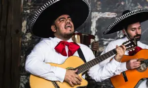 Zespół mariachi w tradycyjnych strojach, z wielkimi kapeluszami i czerwonymi muszkami, gra na gitarach i akordeonie.