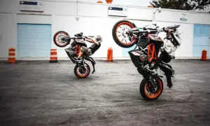 Dwóch motocyklistów wykonuje wheelie na swoich pomarańczowych motocyklach.