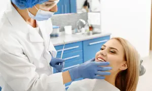 Dentystka bada uśmiechniętą pacjentkę, by wykluczyć zapalenie okostnej i ropień zęba.