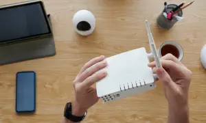 Ręce trzymają biały router, obok tablet, telefon i kubek herbaty. Czas na konfigurację sieci i hasło do sieci wifi.