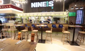 Wnętrze restauracji Lewandowskiego "NINE9S" z barem, stołkami i stołami.