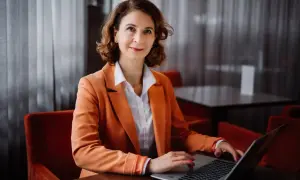 Kobieta w pomarańczowej marynarce pracuje na laptopie w eleganckim wnętrzu.