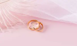 Dos anillos de oro rosa entrelazados, sobre un fondo rosa pálido con una pluma blanca y tela delicada.