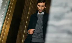 Elegancki mężczyzna w szarym swetrze męskim z warkoczowym splotem, pod ciemną marynarką. Stylowa inspiracja, jak nosić sweter męski.