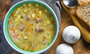 Aromaticzny krupnik, przepis babci, z kawałkami mięsa, ziemniaków i marchewki, posypany koperkiem. Obok kromki chleba i solniczki.