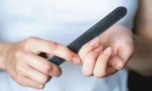 Dłonie z naturalnymi paznokciami, które są piłowane pilniczkiem. Zastanawiasz się, ile warstw ma paznokieć?