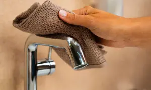 Eine Hand wischt mit einem Tuch über einen glänzenden Wasserhahn, um ihn zu polieren und die Armatur zu entkalken.