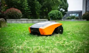 Robot cortacésped autónomo de color naranja y negro, listo para mantener impecable el césped artificial de un jardín moderno.