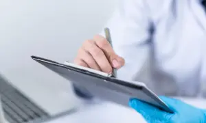 Lekarz w niebieskich rękawiczkach notuje wyniki badań, w tym poziom kalprotektyny w kale, na tablecie.