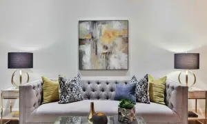 Nowoczesna szara sofa z pikowanymi guzikami, ozdobiona poduszkami i abstrakcyjnym obrazem. To idealne miejsce na relaks, tworzące przytulną atmosferę.