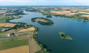 Malowniczy krajobraz Lednickiego Parku Krajobrazowego z wyspami na jeziorze, polami uprawnymi i zabudowaniami.