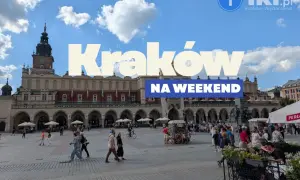 Tłum ludzi spaceruje po Rynku Głównym w Krakowie, ciesząc się piękną pogodą. Widać Sukiennice i wieżę Ratuszową.
