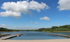 Piękny, słoneczny dzień nad jeziorem Wilczyńskim. Piaszczysta plaża, drewniane pomosty i błękitne niebo z białymi chmurami zapraszają do wypoczynku.