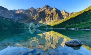Spokojne jezioro odbija skaliste szczyty i zielone zbocza. Idealne miejsce, by zastanowić się, gdzie w Tatry wybrać się na wędrówkę.