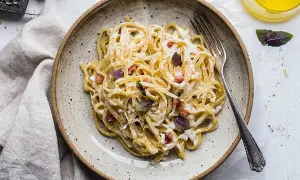 En tallrik med krämig, klassisk carbonara, toppad med basilika och parmesan. En gaffel ligger redo att avnjutas.