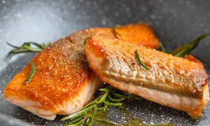 Zwei perfekt gebratene Lachsfilets ohne Haut, garniert mit Rosmarin, liegen in einer Pfanne.