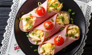 Roladki z szynki z jajecznicą i szczypiorkiem, ozdobione pomidorkami koktajlowymi.