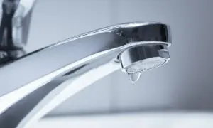 Ein glänzender Chrom-Wasserhahn, bei dem ein einzelner Tropfen Wasser langsam herunterfällt. Der Wasserhahn tropft.