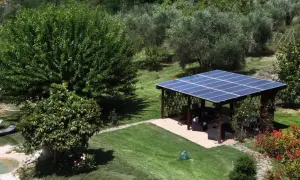 Un pergolato con pannelli fotovoltaici a terra in giardino, in linea con la normativa, offre ombra e energia pulita.