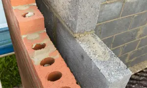 Dettaglio di una parete in costruzione con mattoni rossi forati e blocchi di cemento grigio. Si intravede lo spazio vuoto tra le due murature, ideale per l'**insufflaggio pareti**.