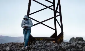 Uomo con fotocamera in cima a un monte san vicino, circondato da rocce e una struttura metallica arrugginita.