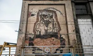 Zniszczony mural w stylu socrealizmu przedstawiający trzech robotników z karabinami.