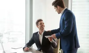 Szef wręcza pracownikowi kopertę, symbolizującą premię uznaniową za świetną pracę.