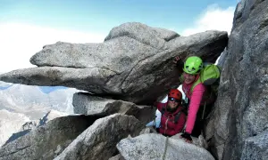 Zwei Bergsteigerinnen auf dem Olperer Nordgrat, lächelnd unter einem Felsvorsprung.