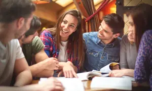 Grupa studentów dyskutuje, stosując 4 zasady aktywnego słuchania. Uśmiechnięta dziewczyna wskazuje na notatki.