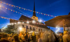 Bunte Girlanden schmücken den Abend bei Weinfeste Franken. Menschen feiern vor einem beleuchteten Gebäude mit Kirchturm.