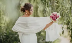 Panna młoda w białej sukni i szalu, trzyma bukiet róż. Idealne co na wierzch do długiej sukienki na wesele.