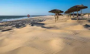 Dunas de arena dorada con sombrillas de paja y un salvavidas, un oasis de paz que recuerda a las playas cerca de Salamanca.