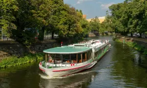 Statek wycieczkowy płynie po zielonej rzece w Berlinie, otoczony drzewami.