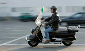 Mężczyzna w kasku i skórzanej kurtce jedzie czarnym motorowerem. To klasyczny pojazd, który wciąż budzi zachwyt.