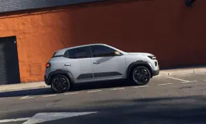 Jasnoszary Dacia Spring na tle pomarańczowej ściany. Sprawdź atrakcyjną dacia spring cena i odkryj jego zalety.