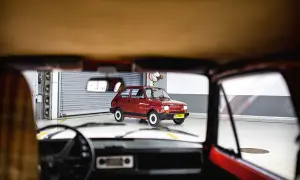 Widok z wnętrza samochodu na lśniącego, **fiat 126p elegant** w kolorze wiśniowym, stojącego w garażu.
