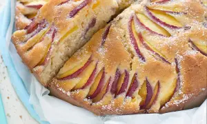 Una fetta di torta di pesche morbidissima, con pesche affettate disposte a raggiera sulla superficie dorata e cosparsa di zucchero a velo.