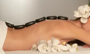 Ciepłe kamienie na plecach kobiety, ozdobione kwiatami, podczas zabiegu SPA.