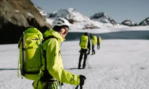 Bergsteiger mit leuchtend gelber Ausrüstung und Rucksäcken auf einer Gletscherwanderung. Die Packliste für die Hochtour ist essentiell für die Sicherheit.