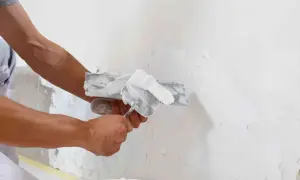 Mani esperte stendono intonaco bianco su una parete, dimostrando che sul polistirolo si può intonacare per una finitura liscia.
