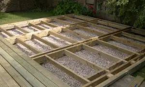 Drewniana konstrukcja pod taras z widocznymi legarami i podsypką żwirową. Wymiary legarów są kluczowe dla stabilności.