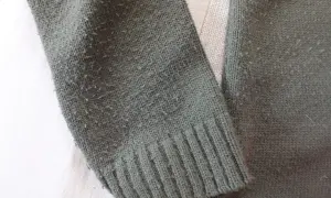 Zielony sweter z dzianiny, na którym widać, czy bawełna się kulkuje. Włókna tworzą drobne kuleczki na powierzchni materiału.