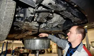 Mechanik spuszcza zużyty olej z samochodu. Pamiętaj o regularnej wymianie oleju w samochodzie co ile, by silnik działał sprawnie.
