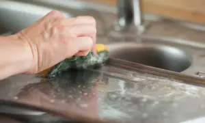 Dłoń z gąbką czyści aluminiowy zlew. Dowiedz się, czym wyczyścić aluminium, by lśniło jak nowe.