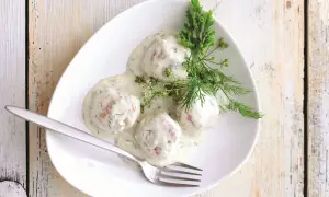 Pyszne pulpety w sosie śmietanowym z koperkiem, podane na białym talerzu z widelcem.