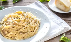 Un piatto di spaghetti fumanti conditi con abbondante cacio e pepe, guarniti con pecorino grattugiato e pepe nero macinato fresco.