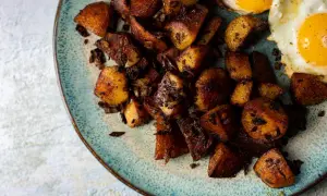 Knusprige bratkartoffeln aus rohen Kartoffeln, goldbraun gebraten, mit zwei Spiegeleiern auf einem rustikalen Teller.